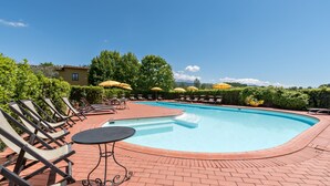 Piscina con sillones de descanso y sombrillas, rodeada de vegetación y un cielo despejado.