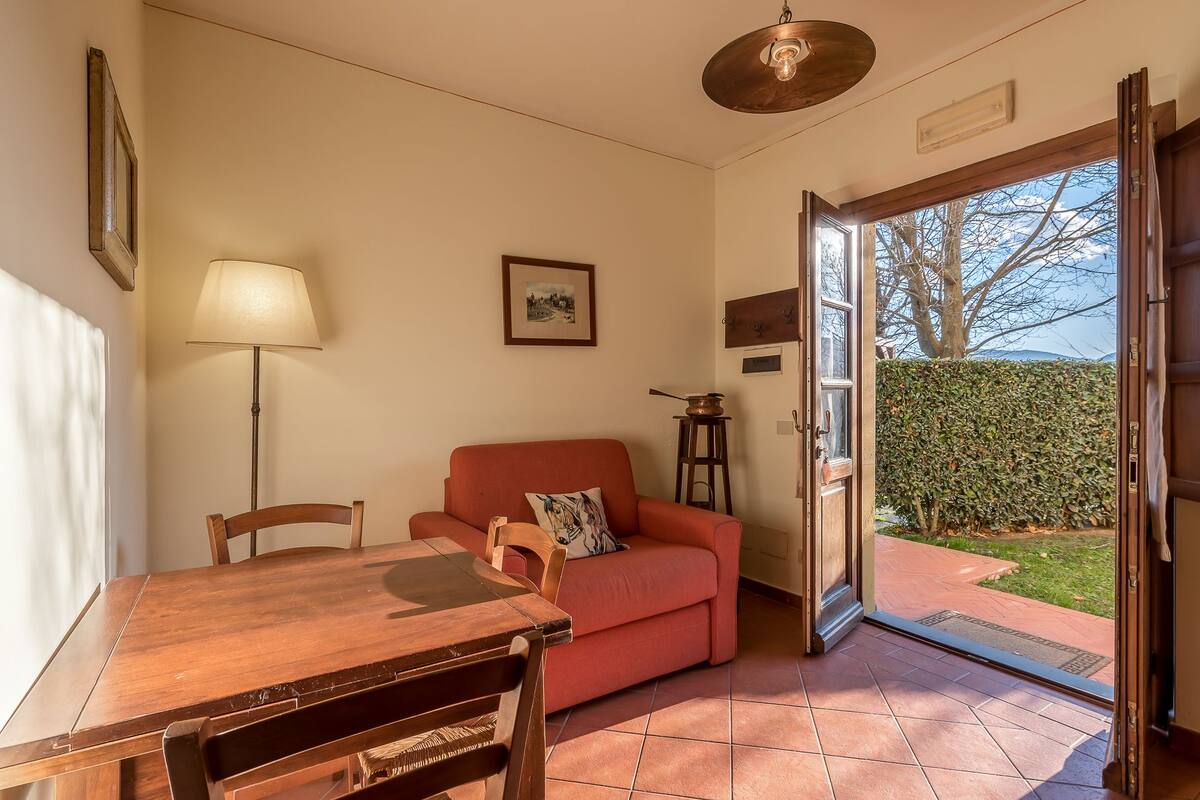 Una habitación acogedora con una mesa de comedor de madera, un sofá rojo y una lámpara. Hay una puerta que da a un jardín.