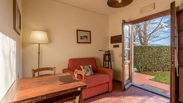 Una habitación acogedora con una mesa de comedor de madera, un sofá rojo y una lámpara. Hay una puerta que da a un jardín.