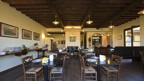 Un comedor con mesas y sillas de madera, una cocina al fondo y cuadros en las paredes.