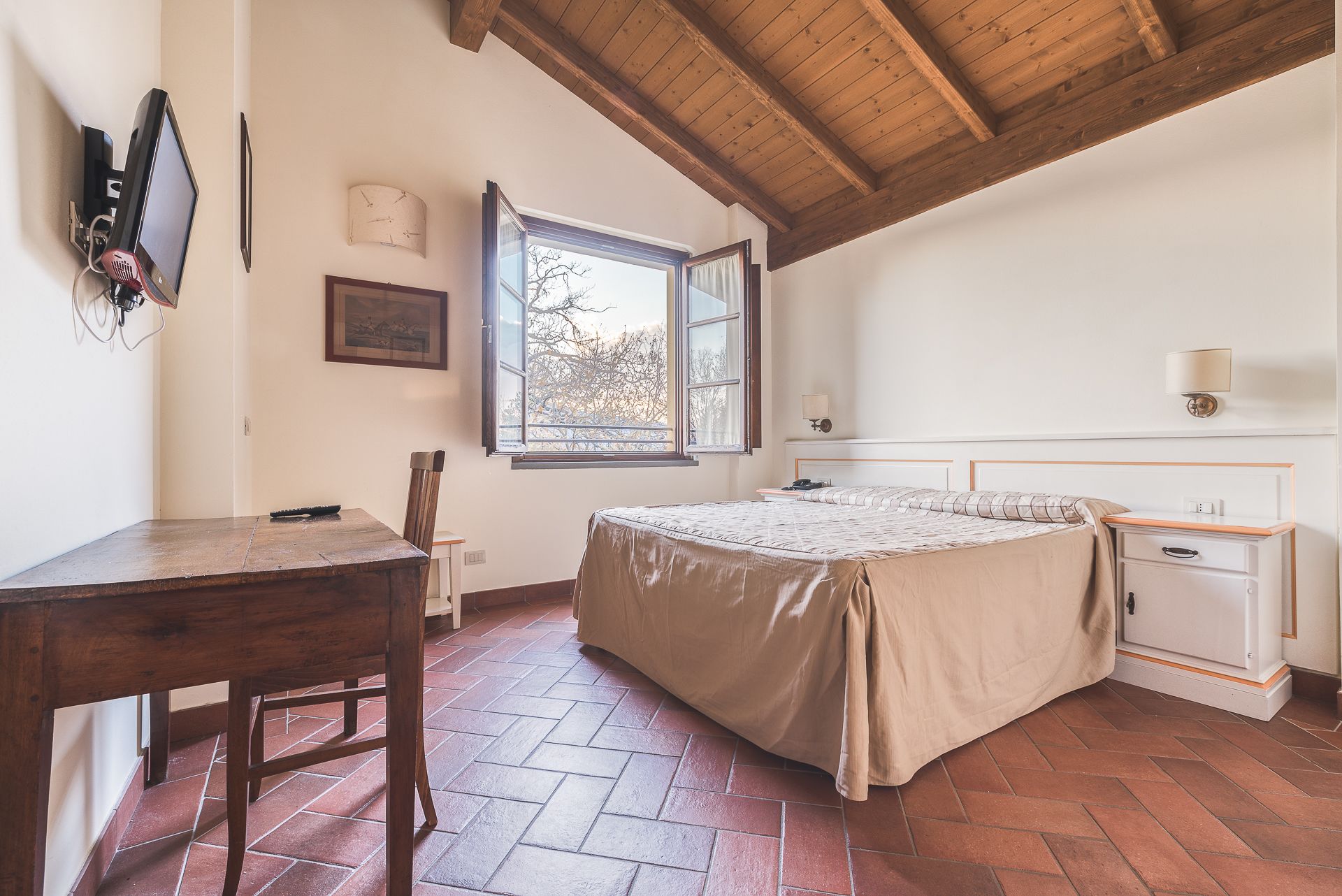Un dormitorio con cama, escritorio, silla, ventana y mesita de noche.