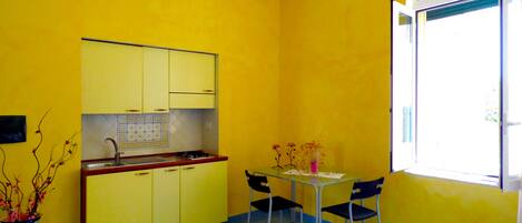 A small kitchen with yellow cabinets, a sink, and a stove. There is a dining table with chairs and a vase with flowers.