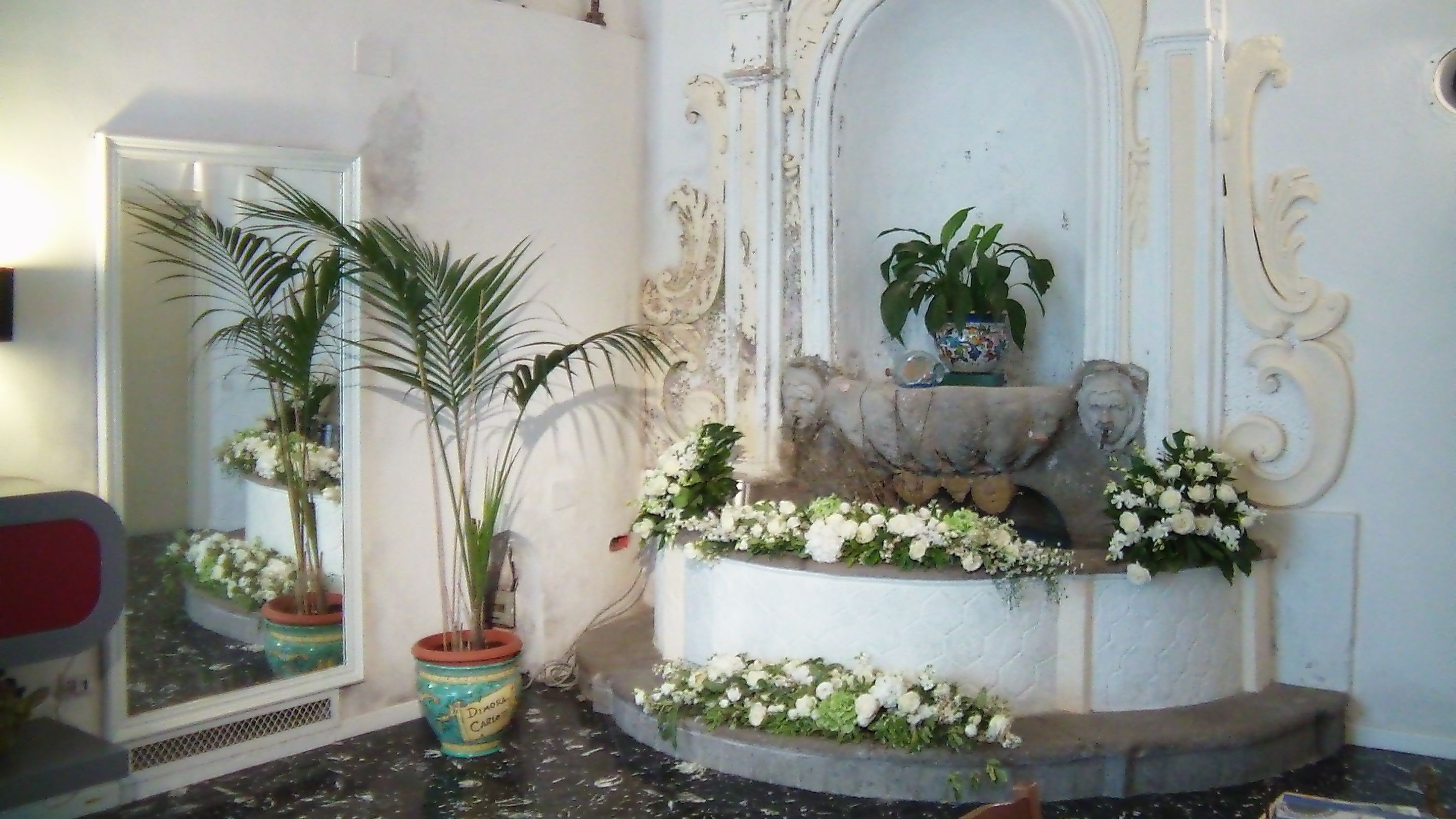 A bathroom with a mirror, a sink, and a decorative fountain with white flowers.