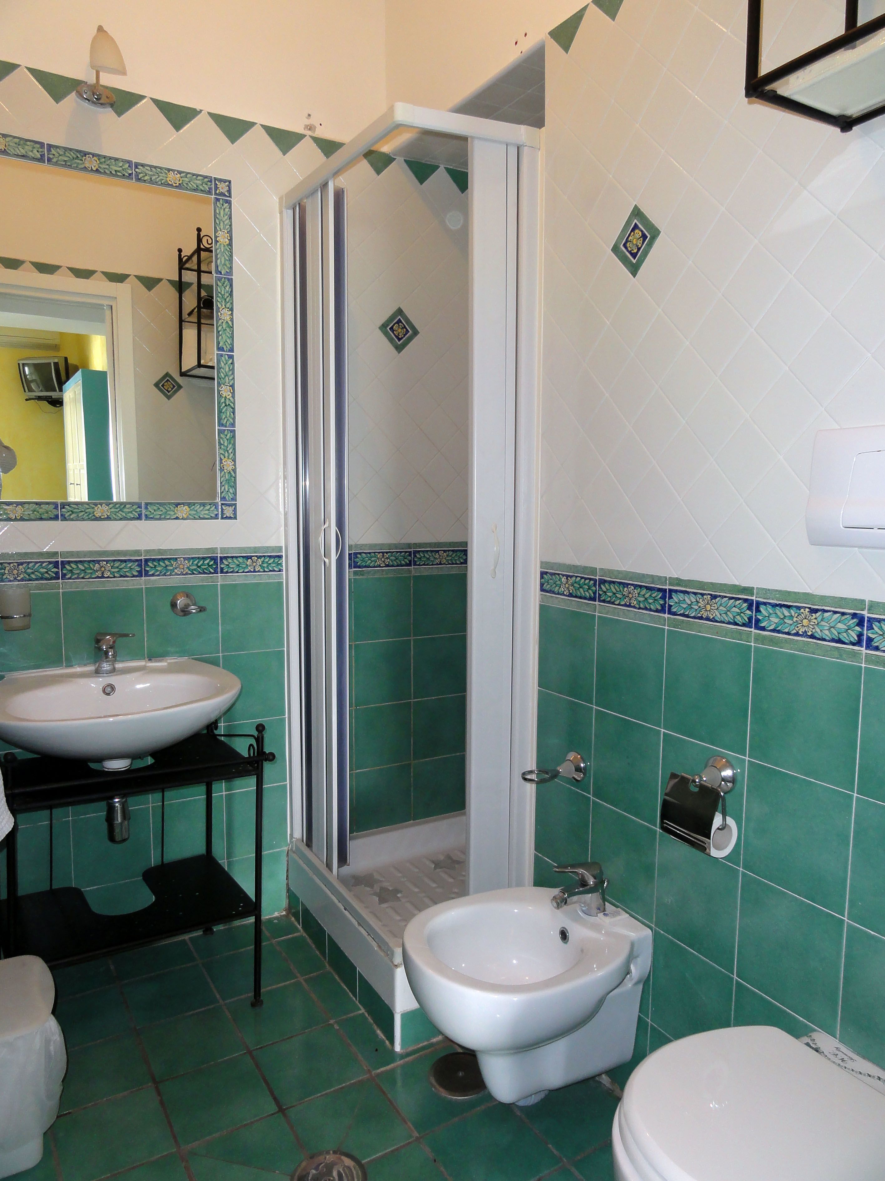 A bathroom with a shower, sink, bidet, and toilet.