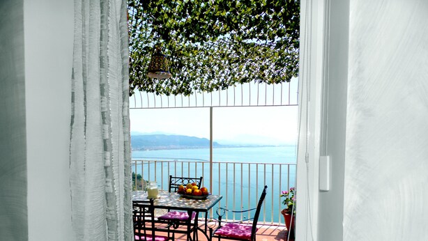 Ein Balkon mit Tisch, Stühlen, einer Obstschale, einer Kanne und einem Blumentopf.
