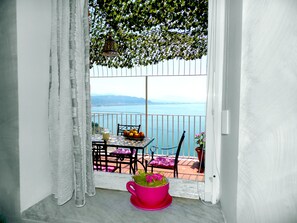 A balcony with a table, chairs, a fruit bowl, a pitcher, and a potted plant.