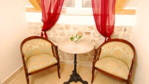 Habitación de esquina con dos sillas de madera, una mesita redonda y un florero con flores.