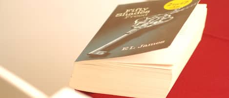 A book titled 'Fifty Shades of Grey' by E.L. James on a red surface.