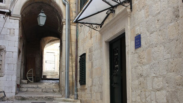 Una estrecha calle adoquinada con un pasaje en arco, una puerta negra y un letrero que indica un hotel llamado "Sorelle".