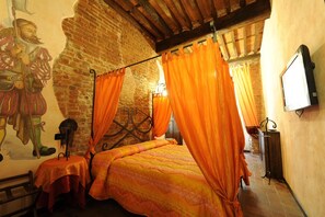 A room with a four-poster bed, orange curtains, a mural on the wall, and a television on the wall. - Antica Corte dei Principi (Lucca)