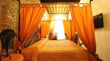 A room with a four-poster bed, orange curtains, a brick wall, and a small table with a chair.