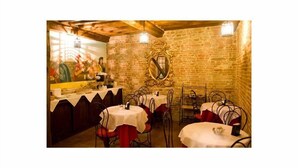 A restaurant with stone walls, wooden beams, and metal chairs. Tables are covered with white tablecloths. - Antica Corte dei Principi (Lucca)