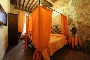 Ein Zimmer mit einem Bett, orangefarbenen Vorhängen, einer Steinwand und einer Holzbalkendecke.