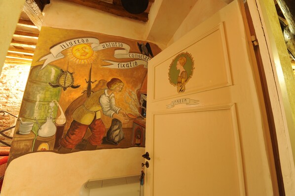 Una habitación con un mural que representa una escena histórica, una puerta con la leyenda 'IPAZIA' y el número '2' en la pared.
