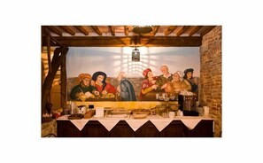 Ein Restaurant mit Wandgemälde einer historischen Szene, Holzbalken und einer Backsteinwand.