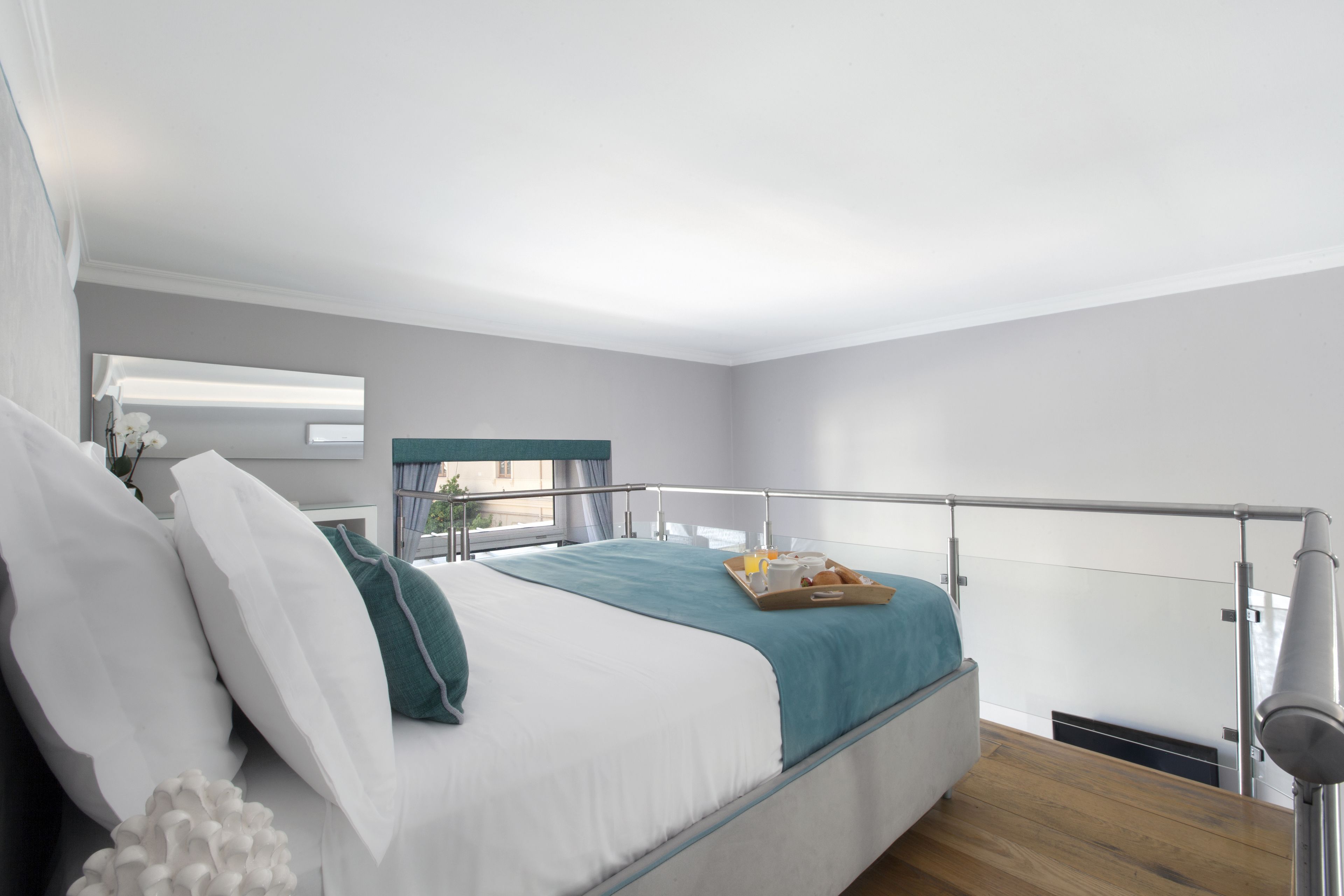 A modern bedroom with a bed, a bedside table, a window with curtains, and a balcony railing.