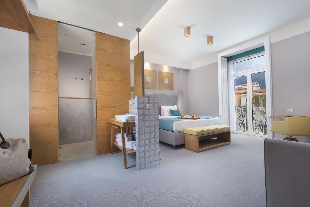 Une chambre d’hôtel moderne, équipée d’un lit, d’une table de chevet et d’une fenêtre donnant sur un paysage agréable.