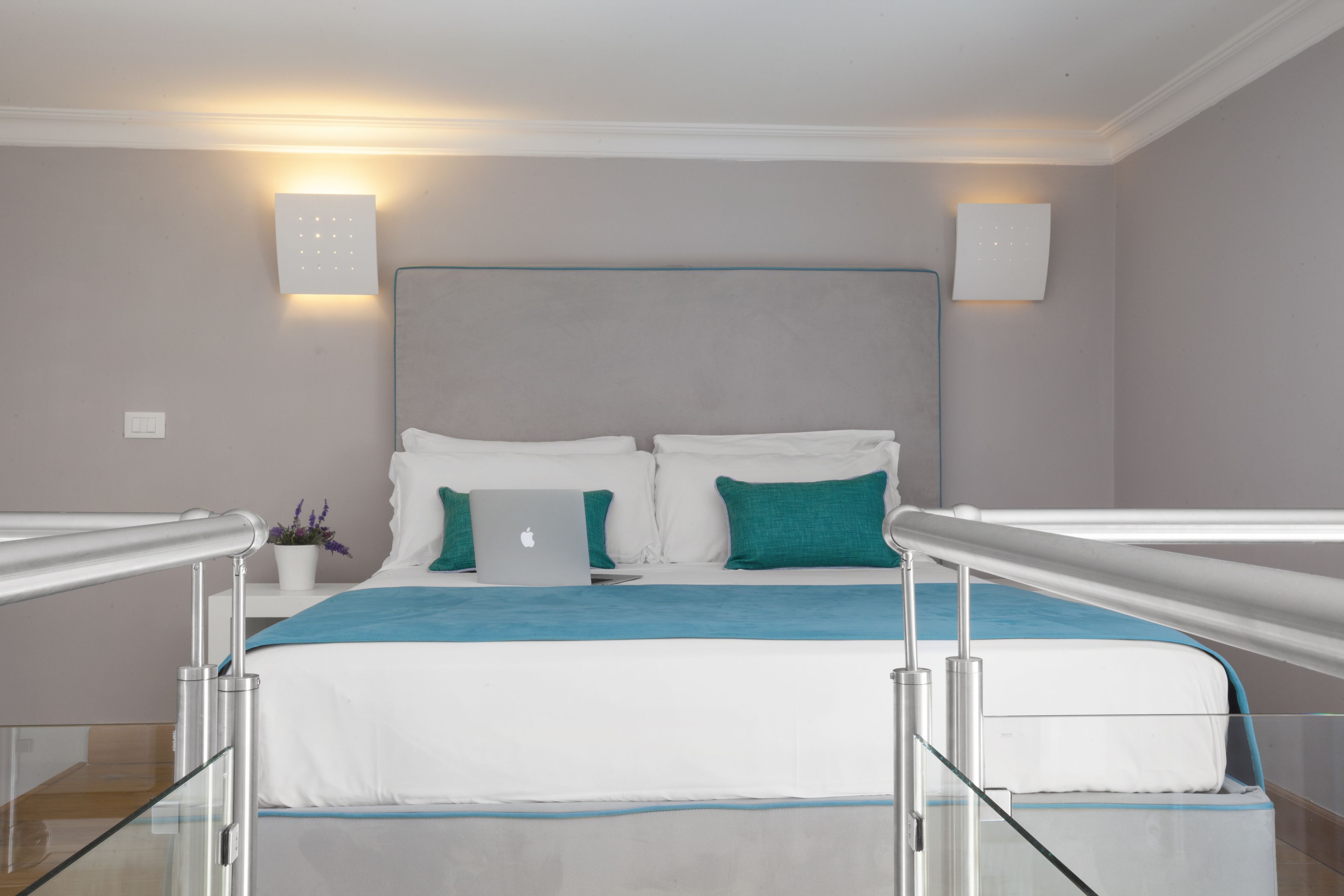 Ein modernes Hotelzimmer mit einem Bett, einem Laptop und einem kleinen Tisch mit einer Pflanze.