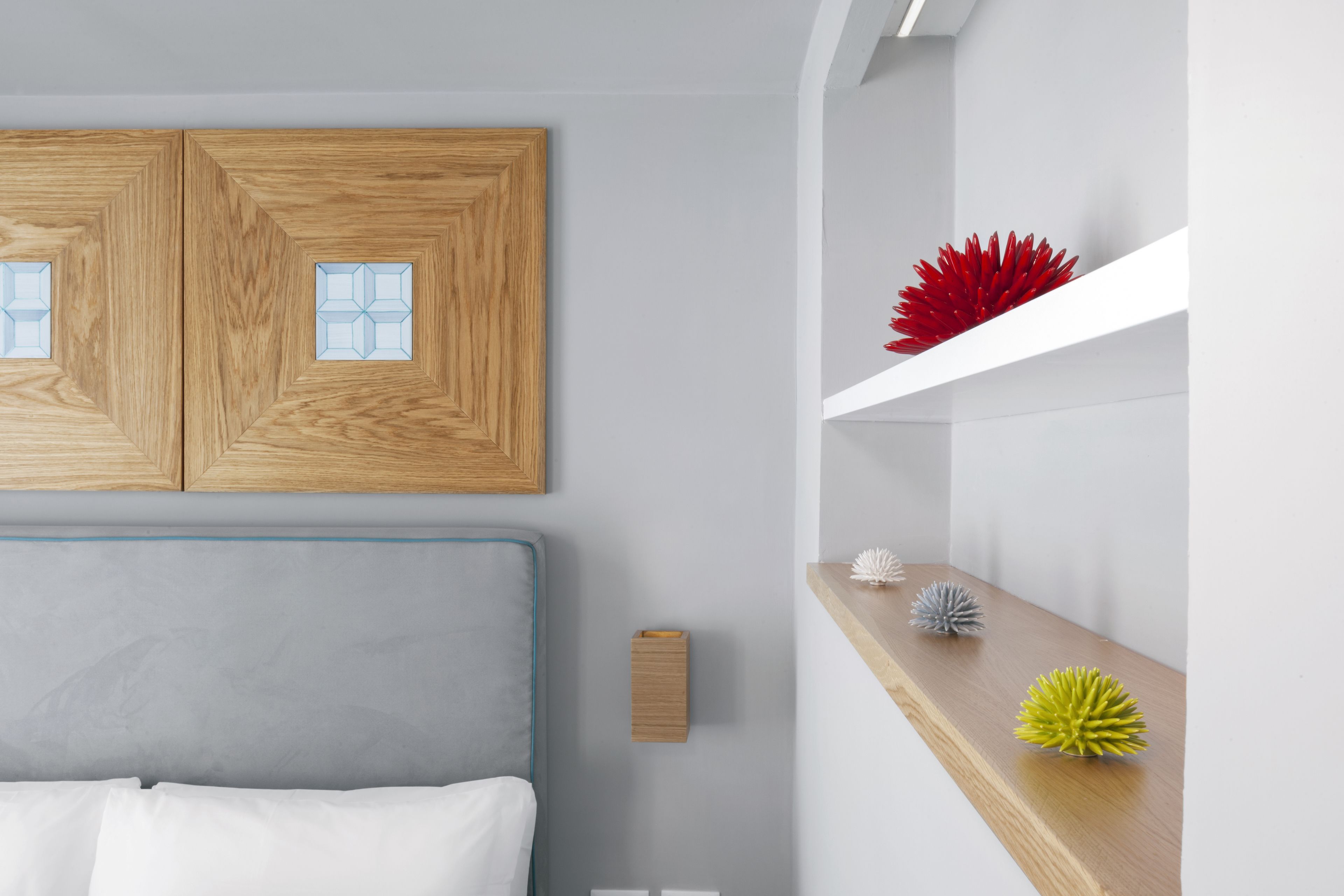 Une chambre moderne avec une tête de lit grise, des panneaux muraux en bois et une étagère blanche agrémentée d’objets décoratifs.
