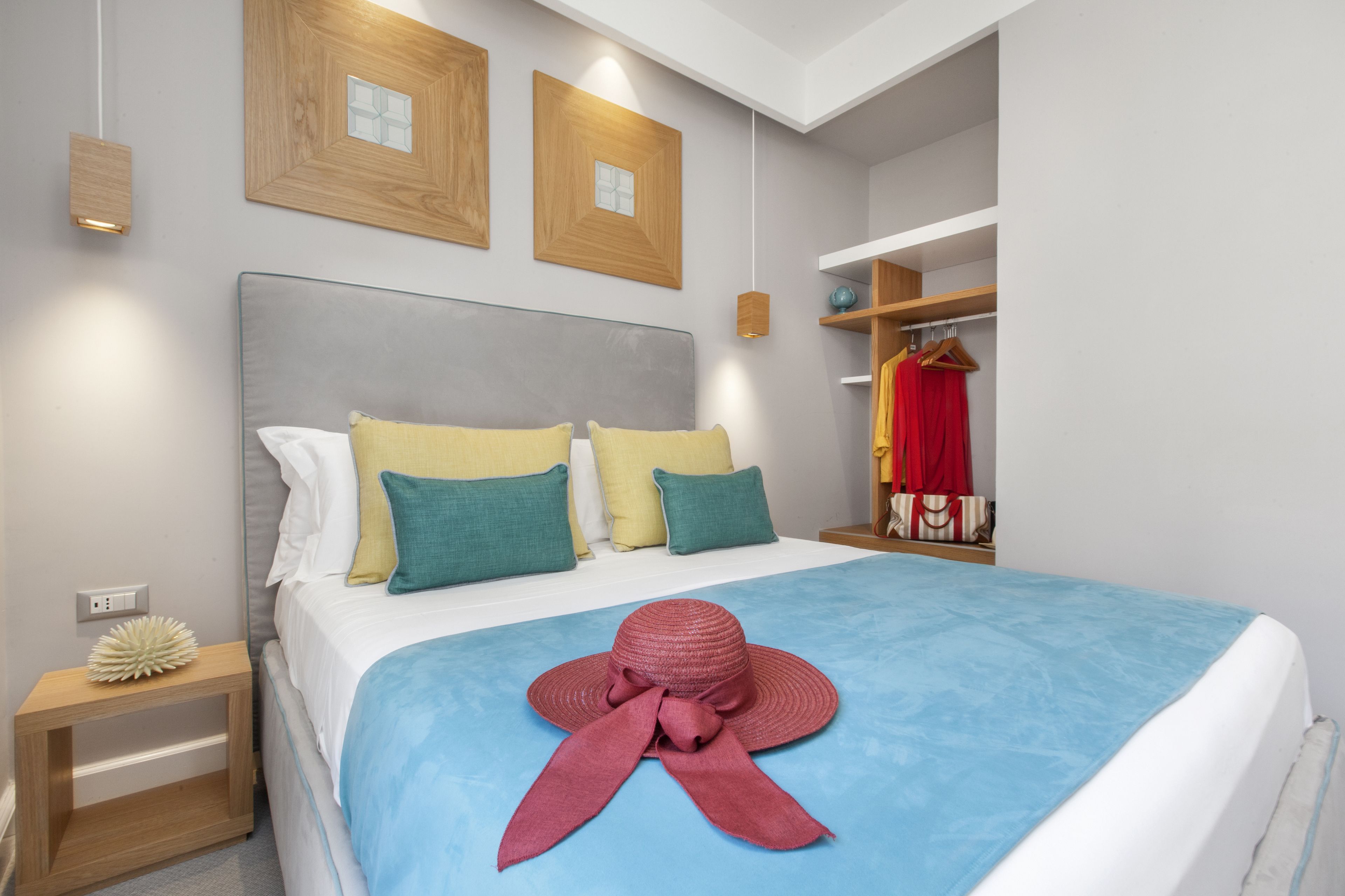 A neatly made bed with a blue bedspread and a red hat on top. There are two wooden picture frames on the wall above the bed.