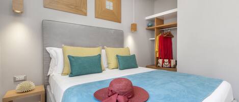 A neatly made bed with a blue bedspread and a red hat on top. There are two wooden picture frames on the wall above the bed.