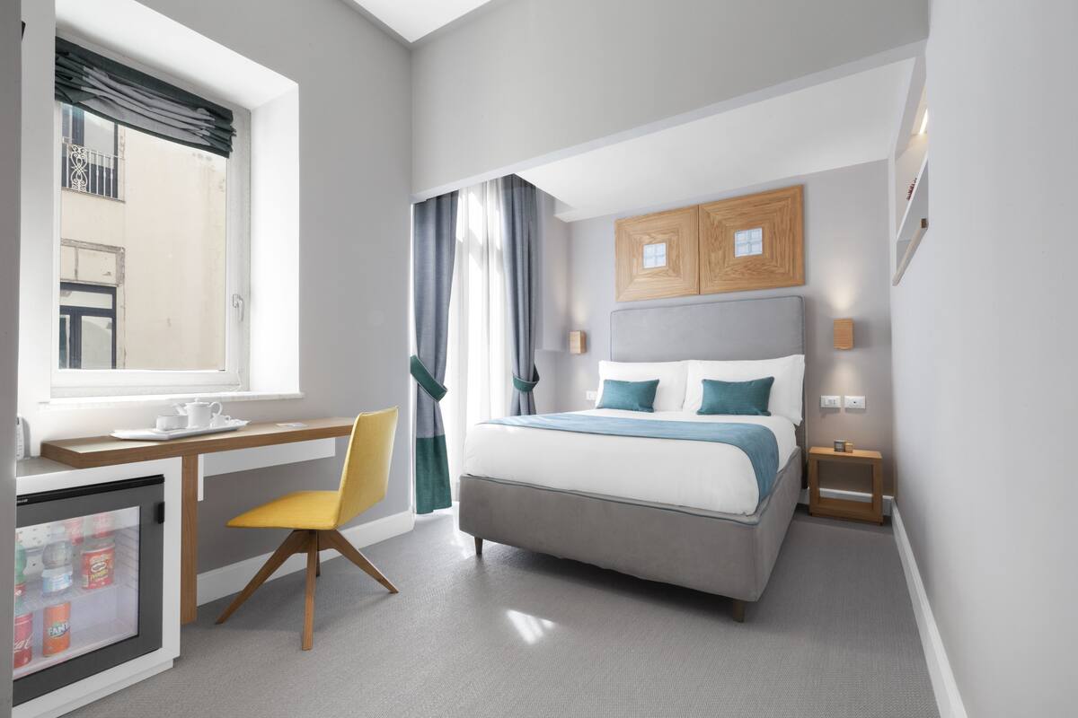 Une chambre d’hôtel comprenant un lit, un bureau avec une chaise, un mini-réfrigérateur et une fenêtre avec des rideaux.