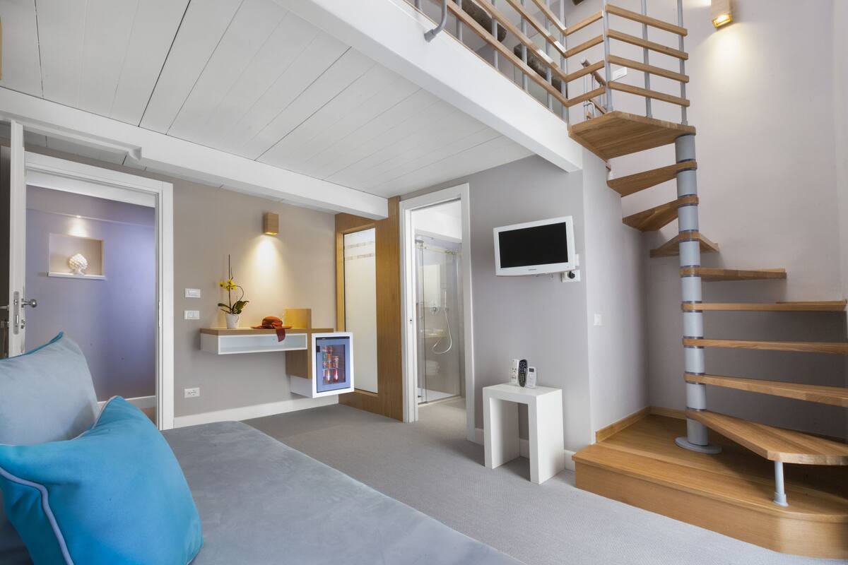 Un intérieur moderne avec un escalier, un téléviseur à écran plat, une petite table et un canapé agrémenté d’un coussin bleu.