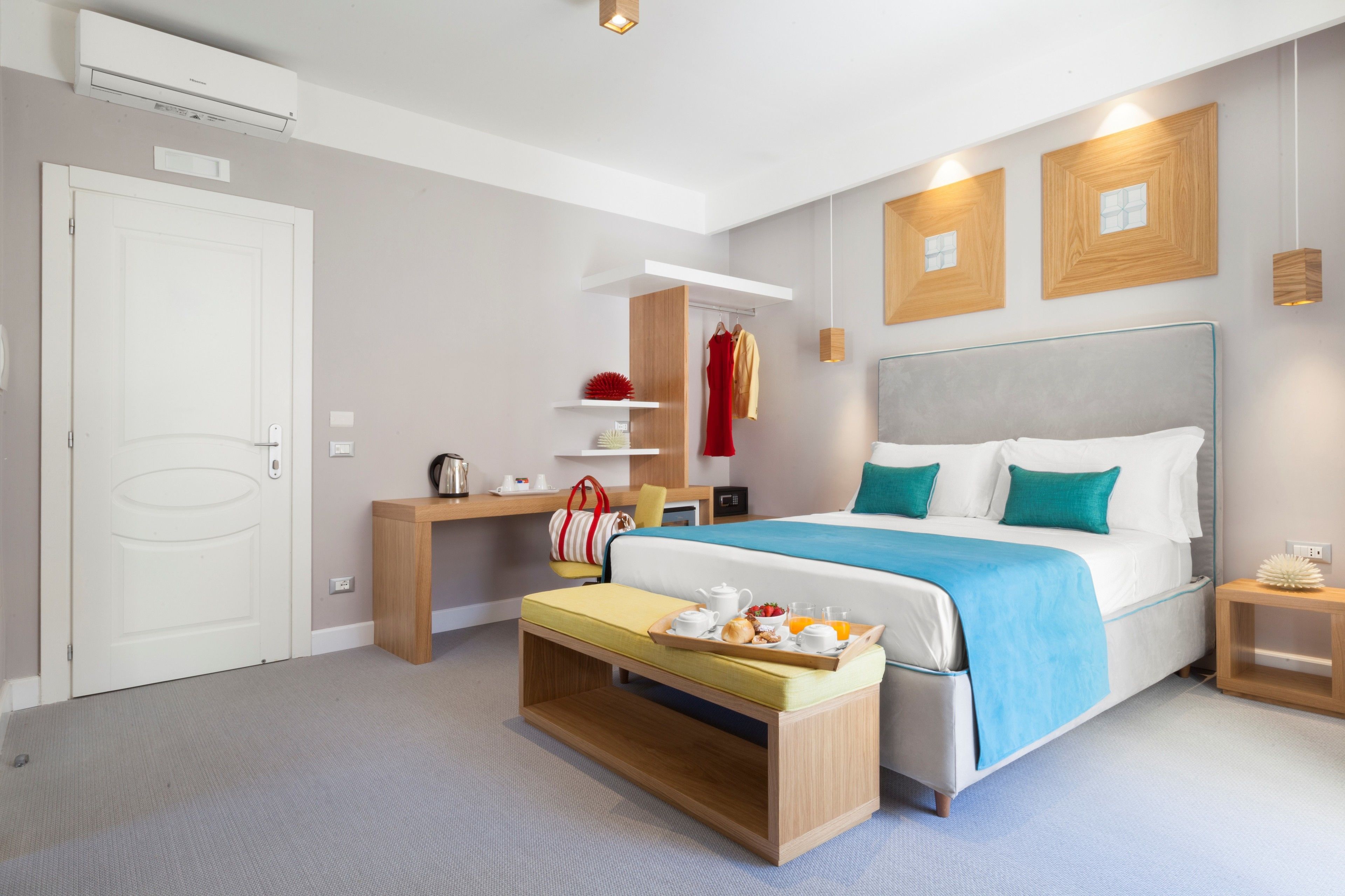 A modern hotel room with a large bed, bedside table, and a small desk with a chair.