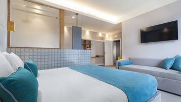 Quarto de hotel moderno com uma cama grande, um sofá, uma televisão de tela plana e um banheiro visível por uma porta aberta.
