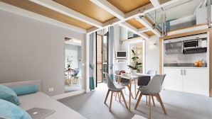 Een moderne woonkamer met een bank, eettafel en stoelen. Er is een keuken met apparatuur en een eettafel.