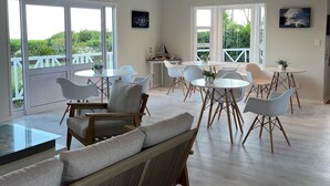 A spacious dining area with modern furniture and large windows offering views of greenery and a bridge. - Brenton Beach House (Knysna)