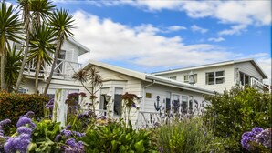 A white house with a balcony, surrounded by various plants and flowers. - Brenton Beach House (Knysna)