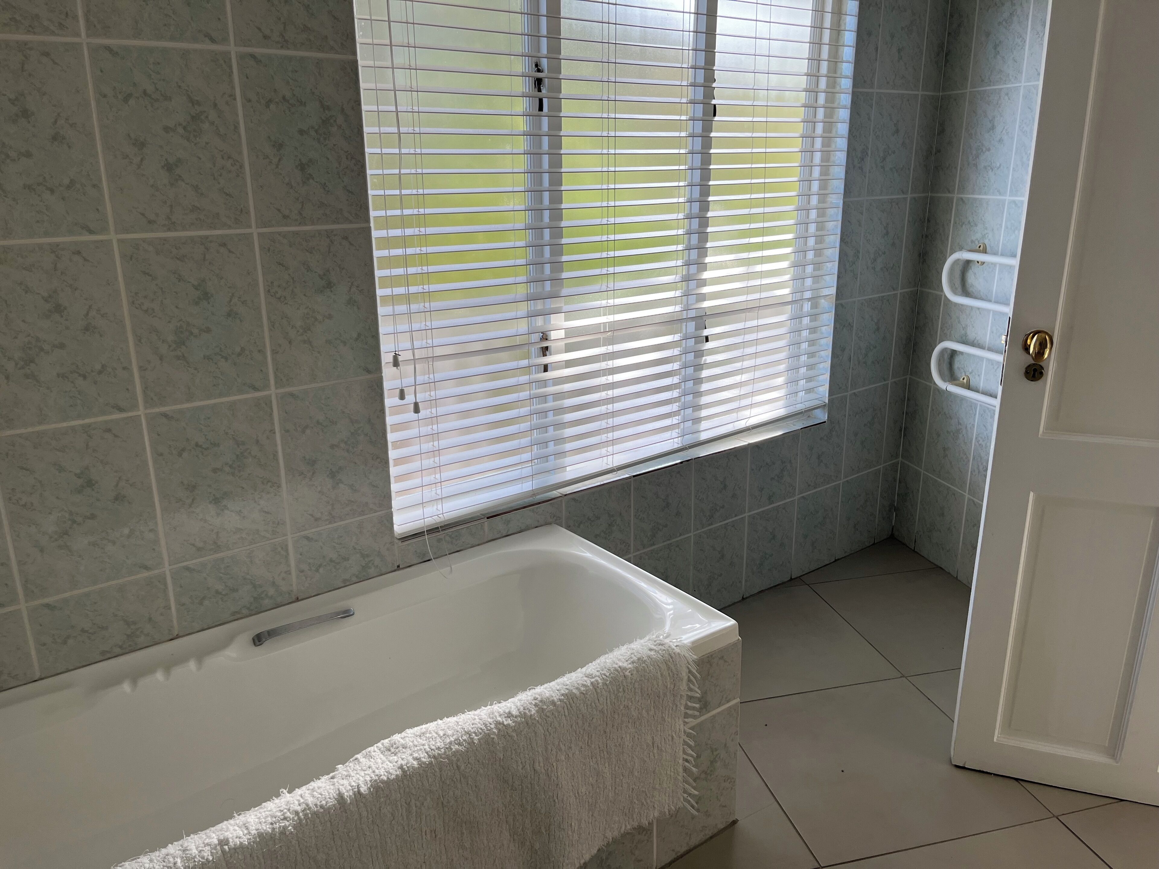 A bathroom with a bathtub, a window with blinds, and a door with a towel rack.