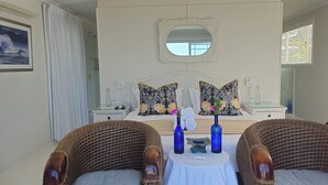 A bedroom with a large bed, two nightstands, a mirror, and wicker chairs. - Brenton Beach House (Knysna)