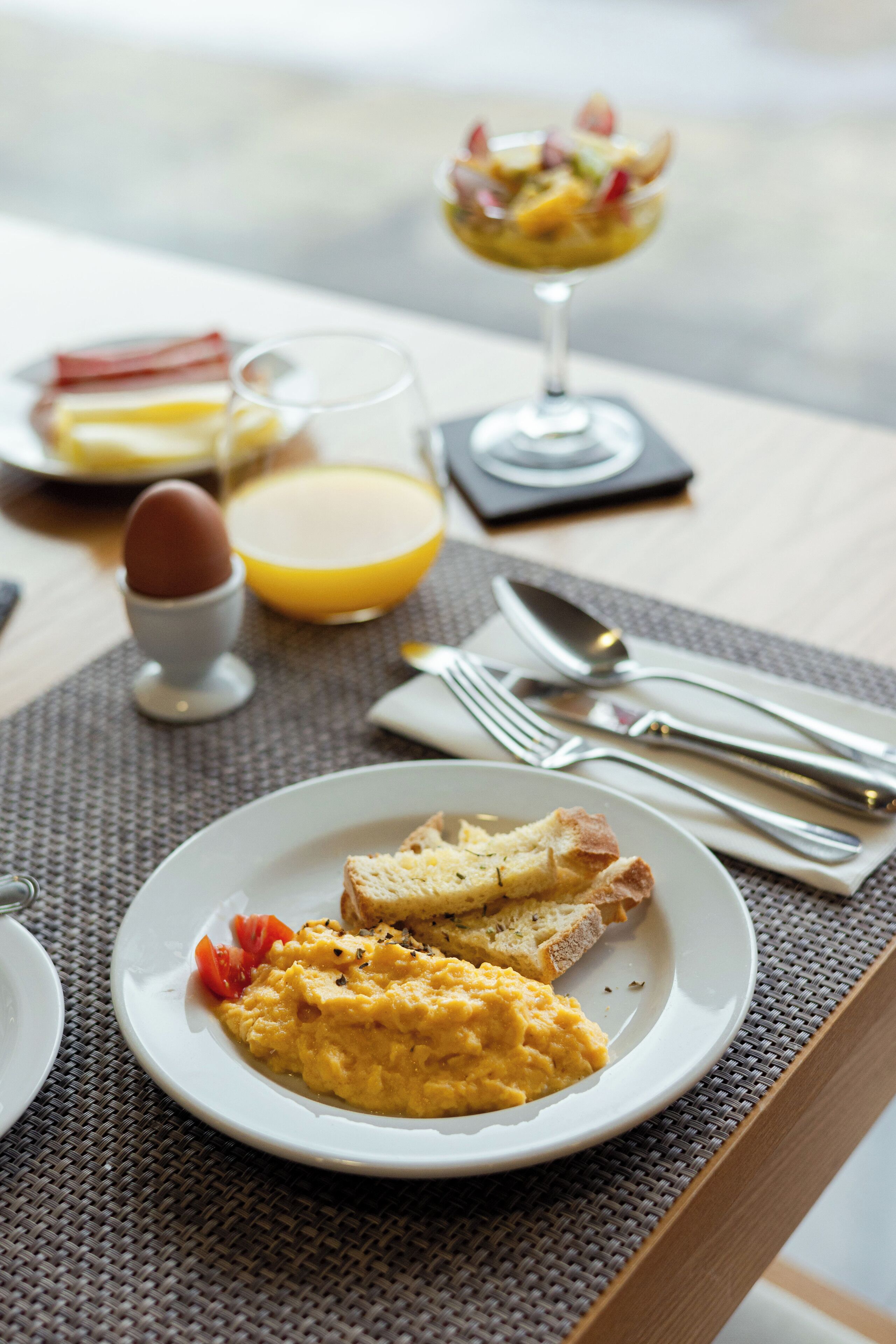 A breakfast setting with scrambled eggs, toast, and a glass of orange juice on a table.