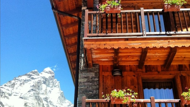 A wooden chalet with a balcony, stone walls, and potted plants. - Hotel Mon Reve (Valtournenche)