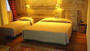 A room with two single beds, wooden walls, a small rug, and two bedside lamps. - Hotel Mon Reve (Valtournenche)