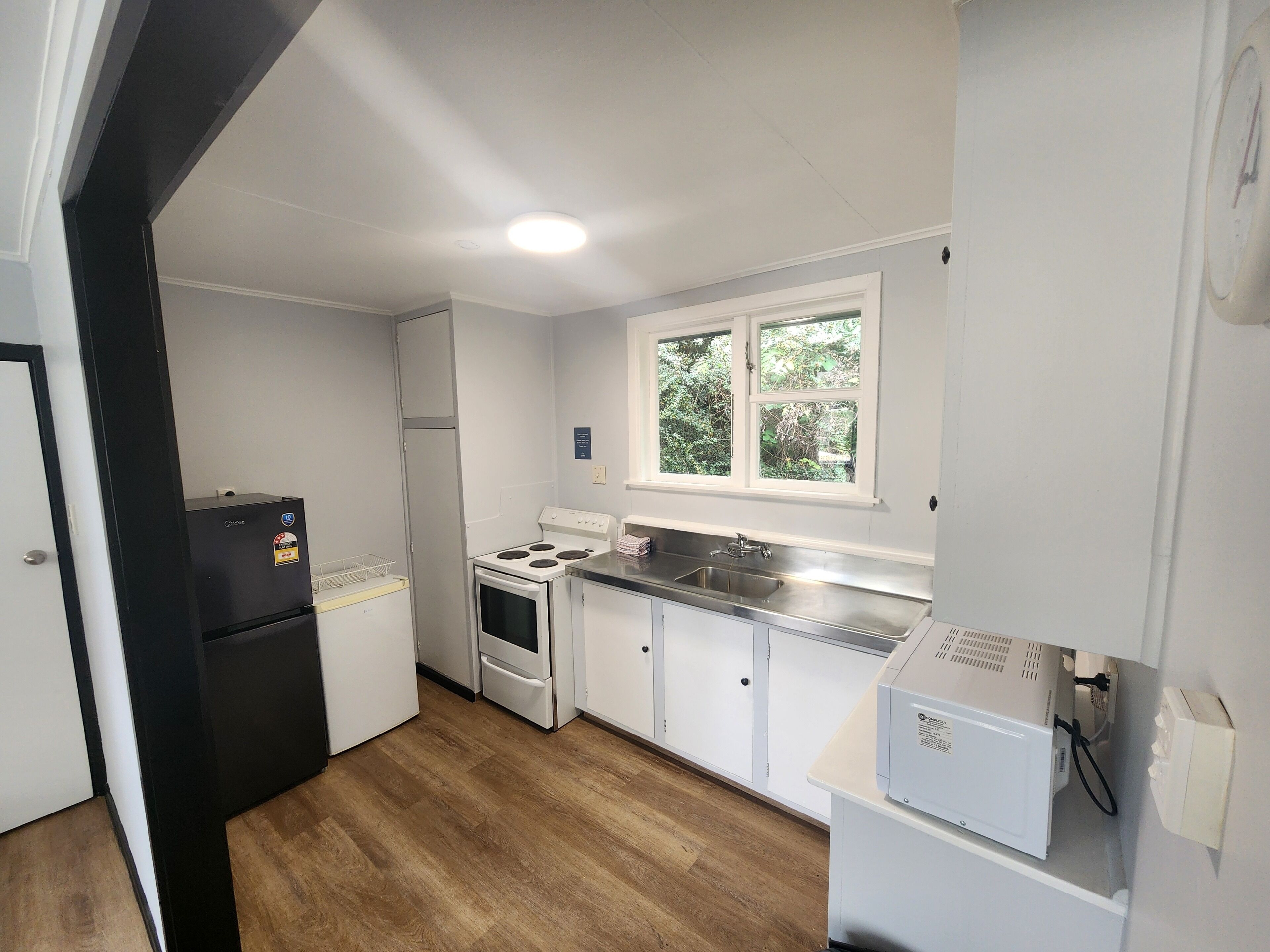 A compact kitchen with white cabinets, a stove, a refrigerator, and a window providing a view of greenery outside.