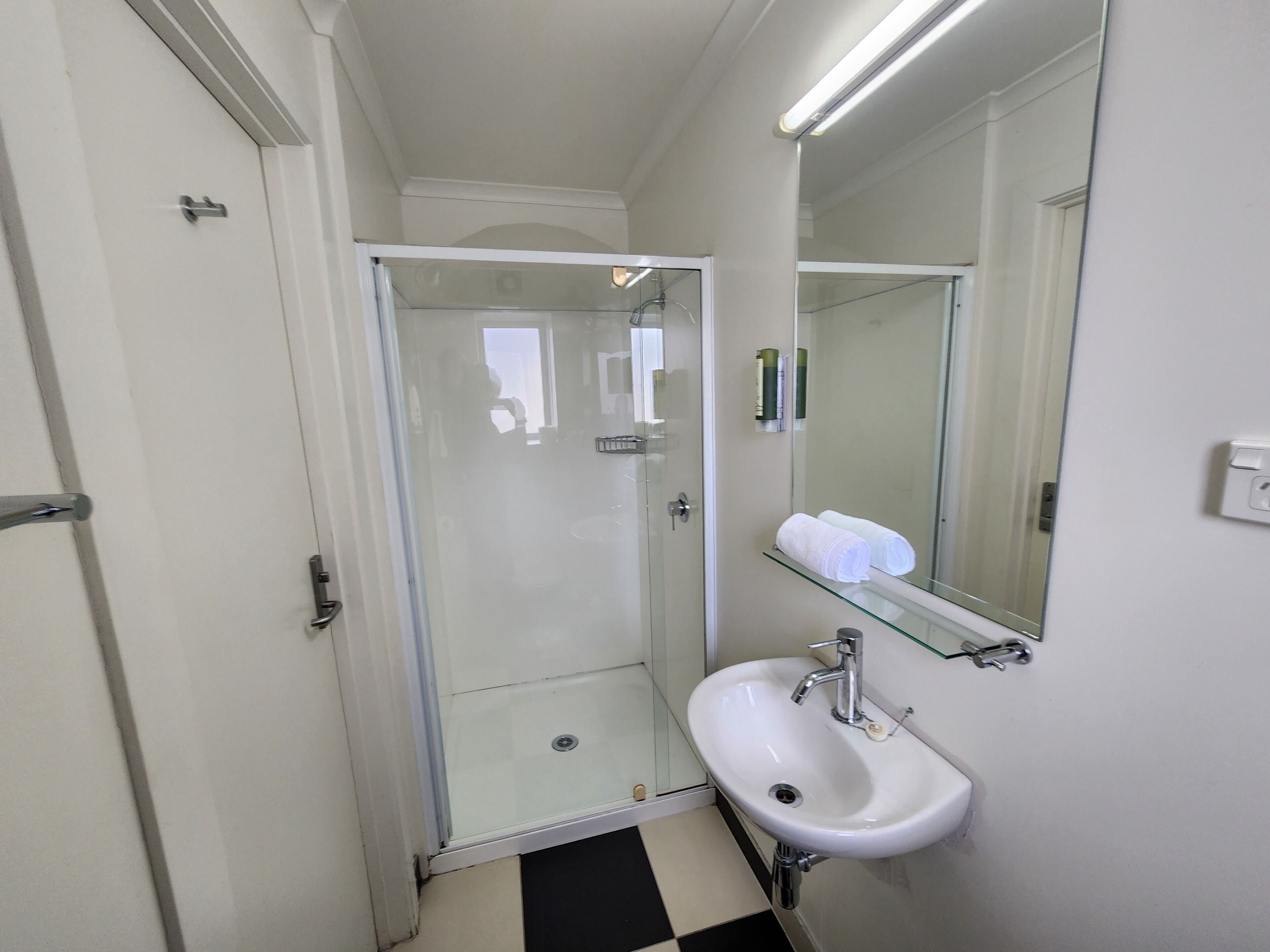 A small, modern bathroom with a glass shower enclosure, a white sink with a mirror above it, and a black and white checkered floor.