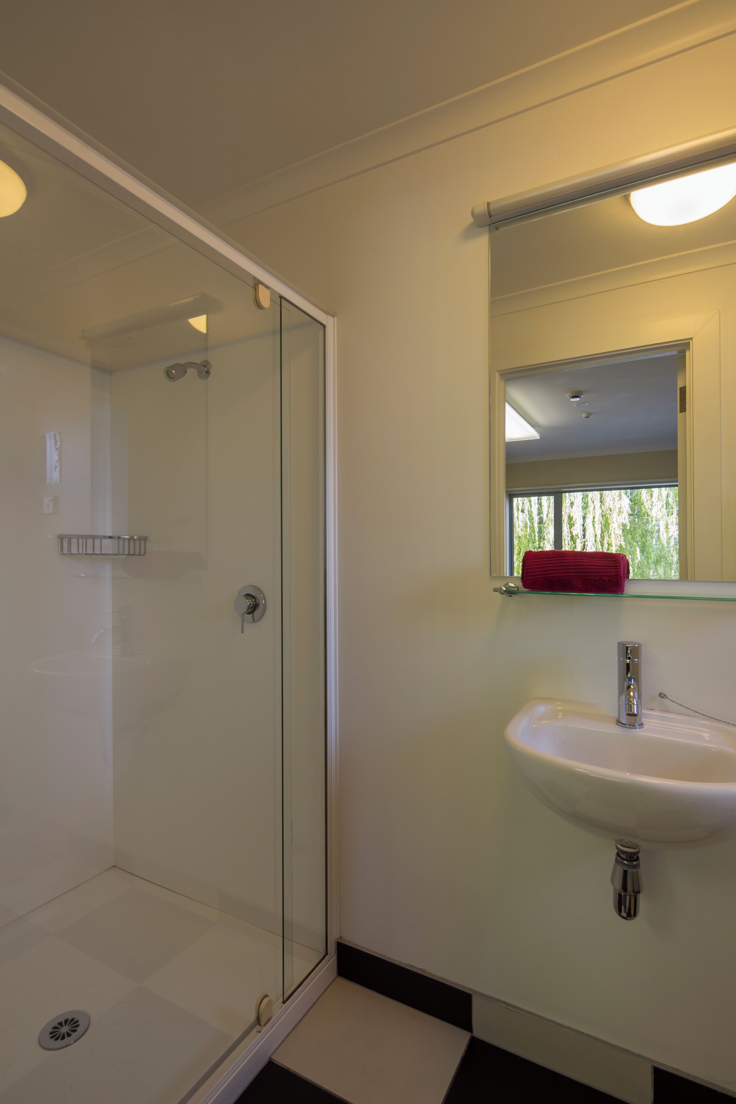 A bathroom with a glass shower enclosure, a white sink, and a mirror with a red towel hanging on it.