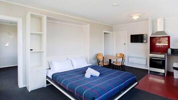 A compact hotel room with a bed, a small kitchenette, a dining area, and a TV.