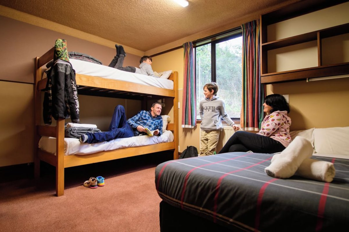 A dormitory room with bunk beds, a single bed, and a window with curtains.