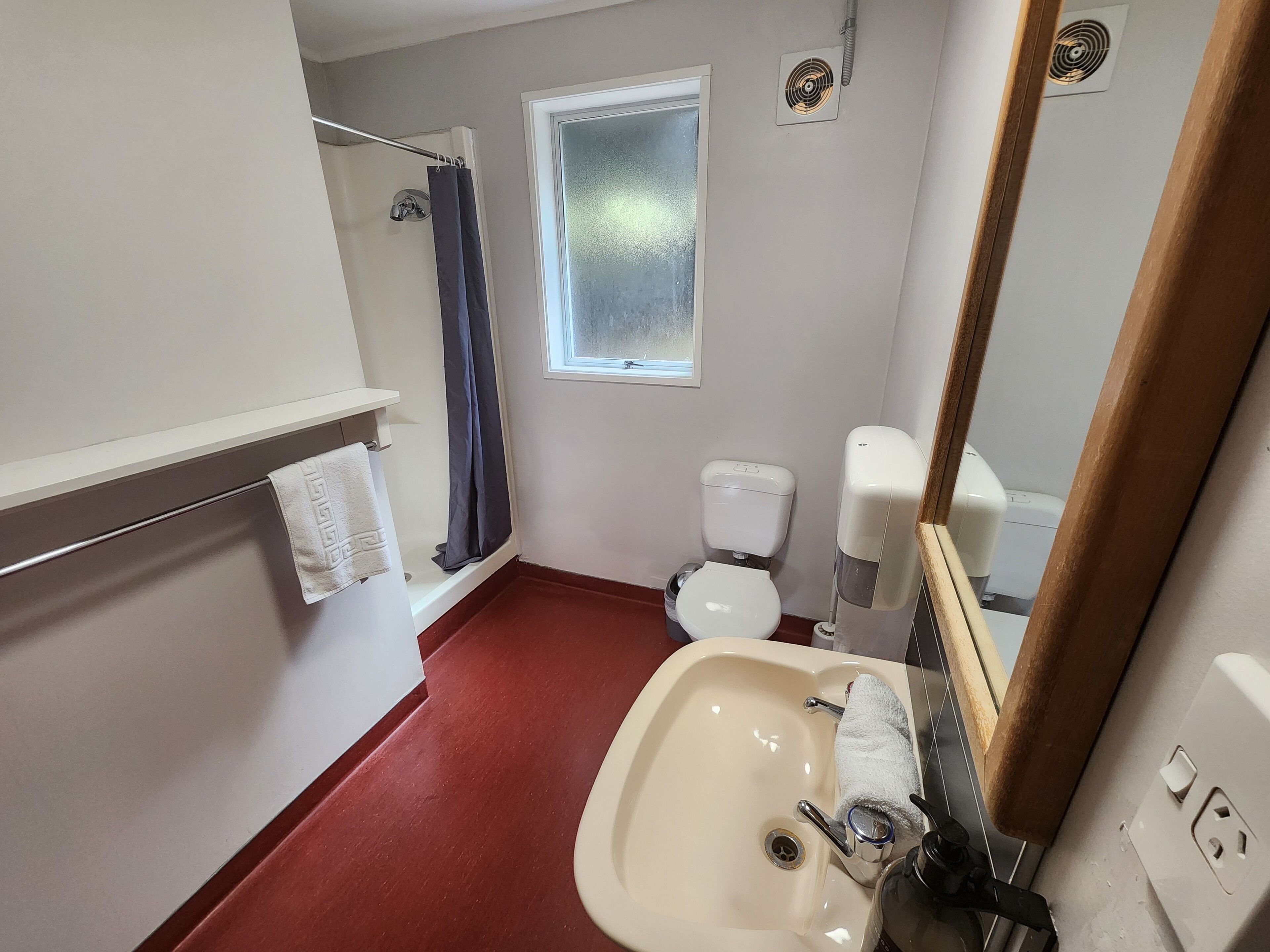 Un baño con lavamanos blanco, inodoro, cortina de ducha, ventana y espejo.