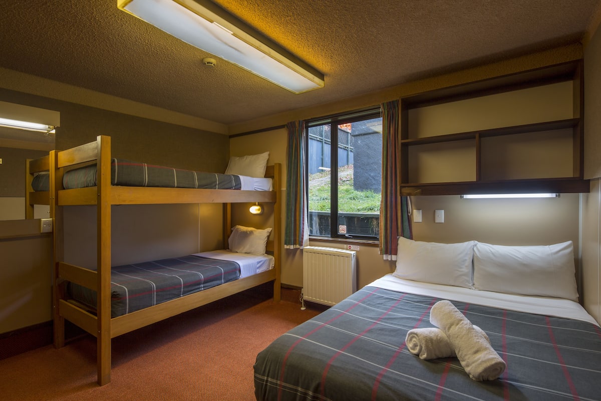 A room with bunk beds, a single bed, and a window with curtains.