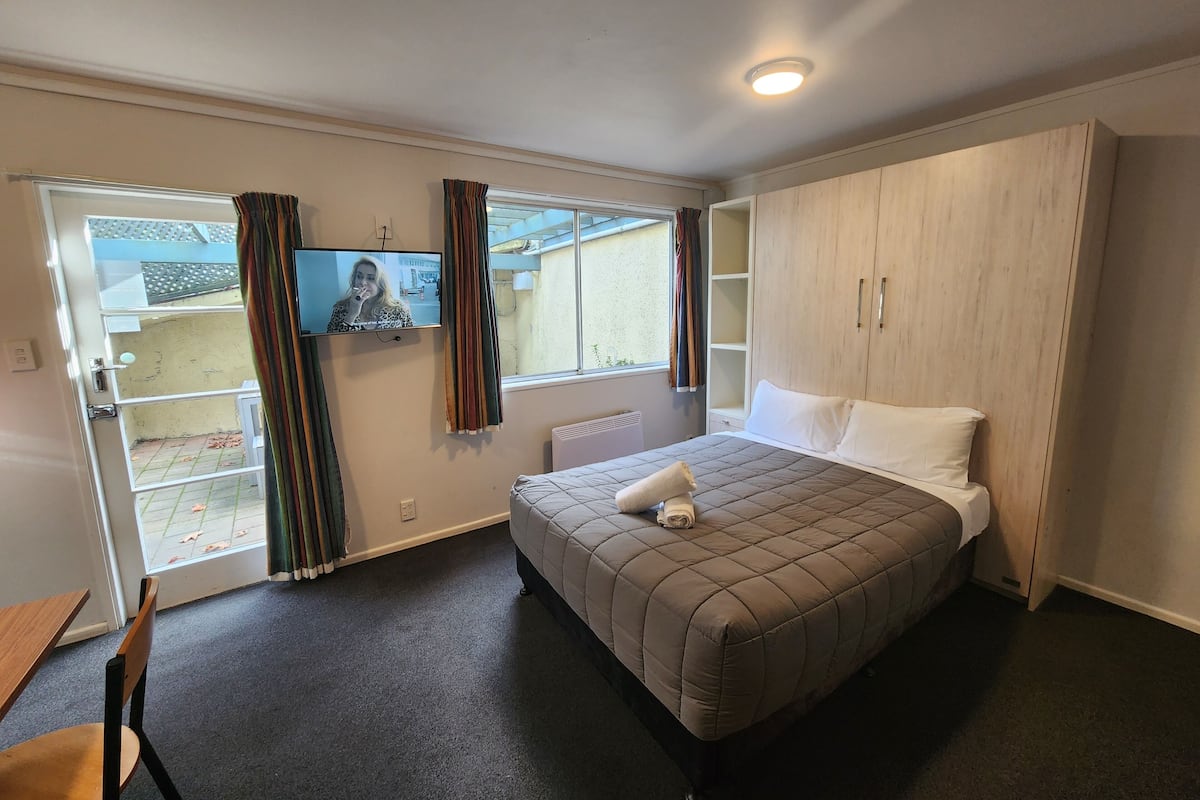 A bedroom with a bed, a TV, a wardrobe, and a window with curtains.