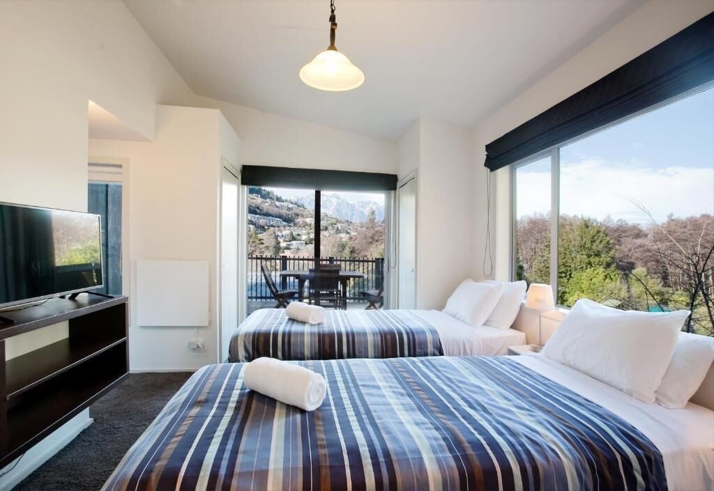 Habitación de hotel con dos camas, televisión y balcón con vistas a montañas.