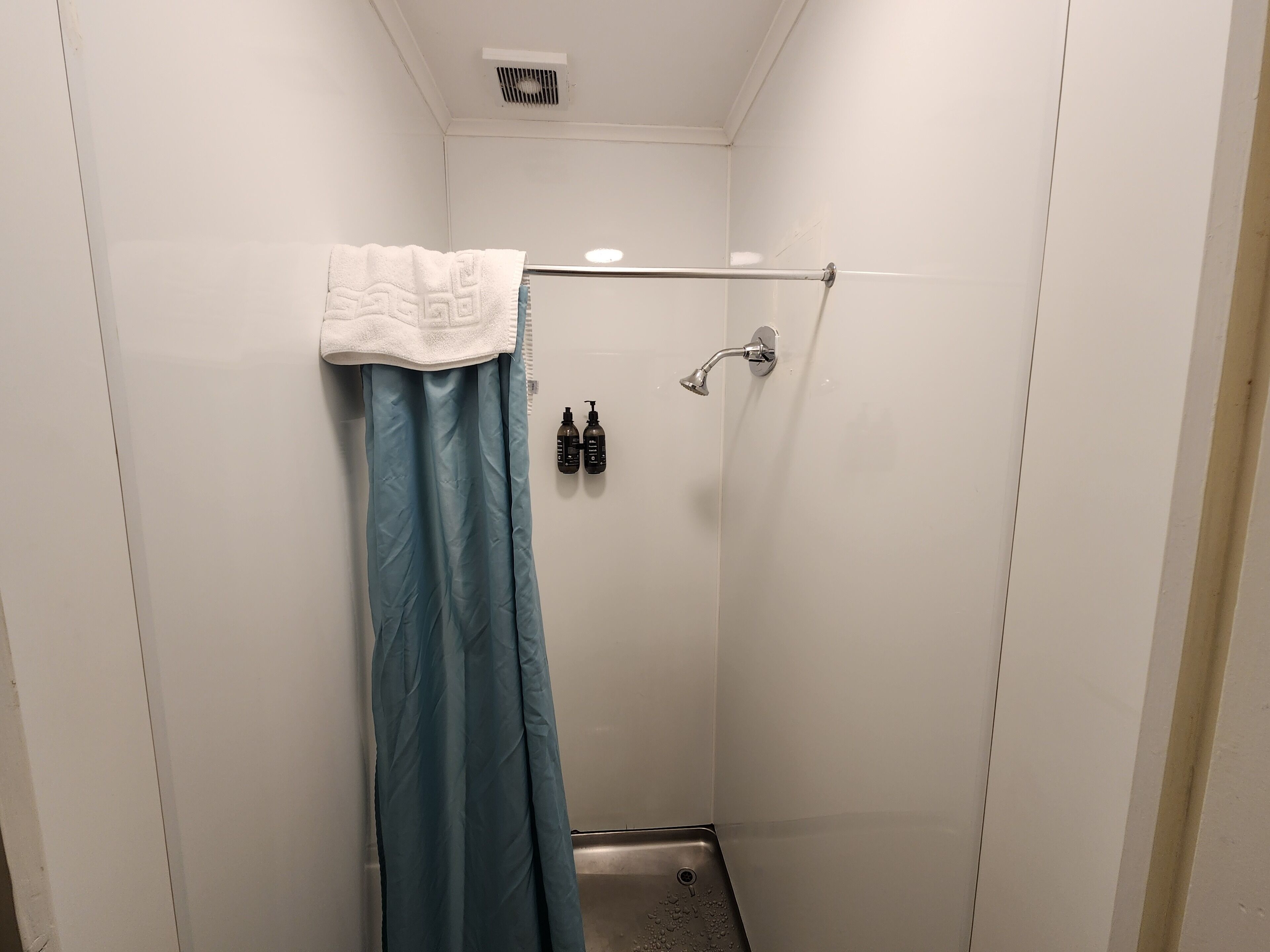 A small, enclosed shower area with a blue shower curtain, a white towel, and two bottles of shampoo and conditioner on the wall.