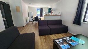 En moderne stue med en mørk sofa, et sofabord med magasiner og et spiseområde med stole og bord.
