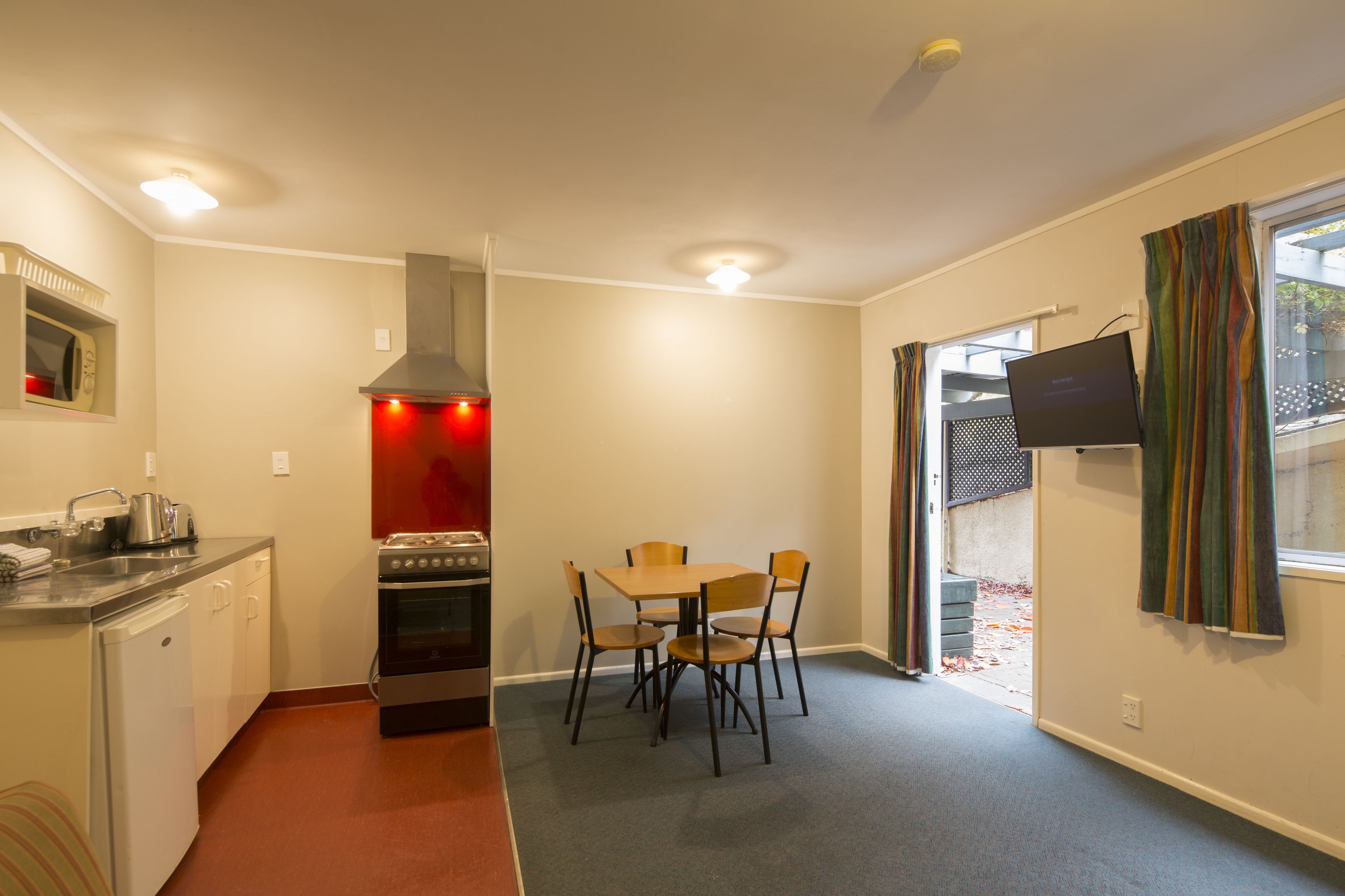 Una cocina compacta con comedor, horno empotrado y televisor en la pared.