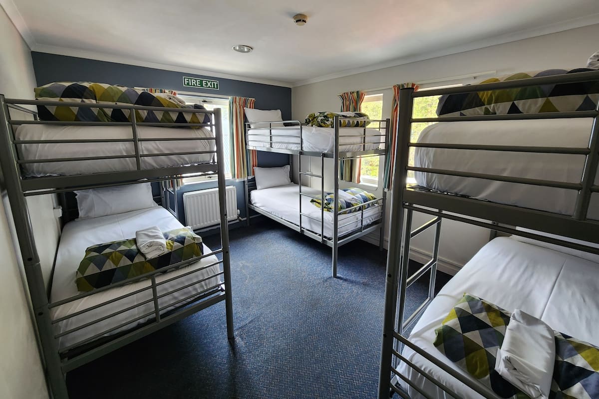 A dormitory room with bunk beds, a fire exit sign, and a window with curtains.
